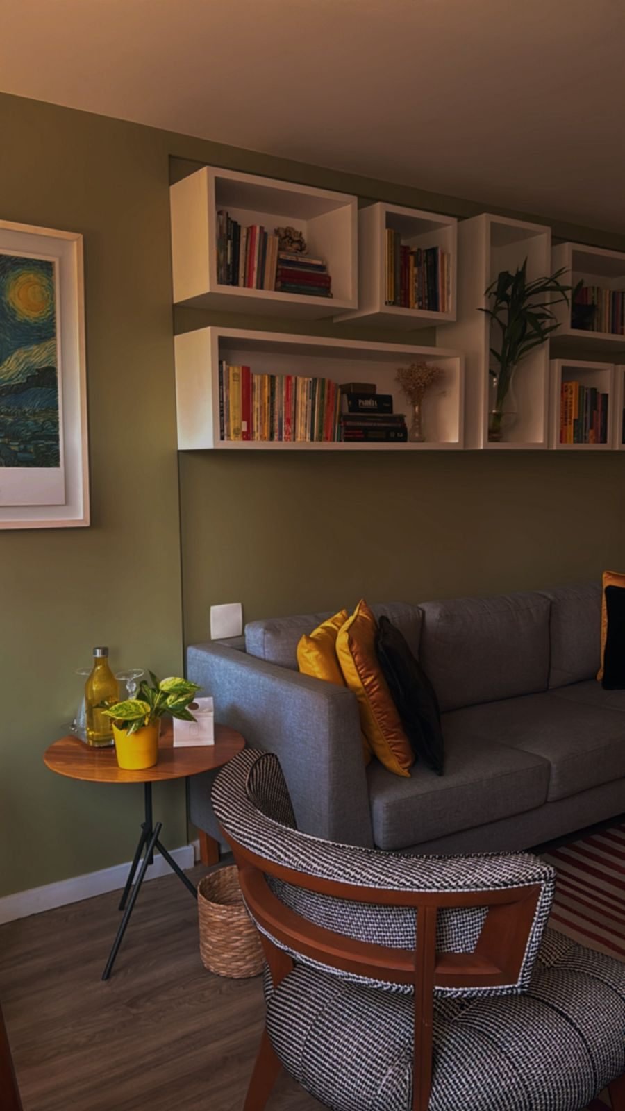 Consultório com sofá cinza, poltrona, estantes de livros e plantas